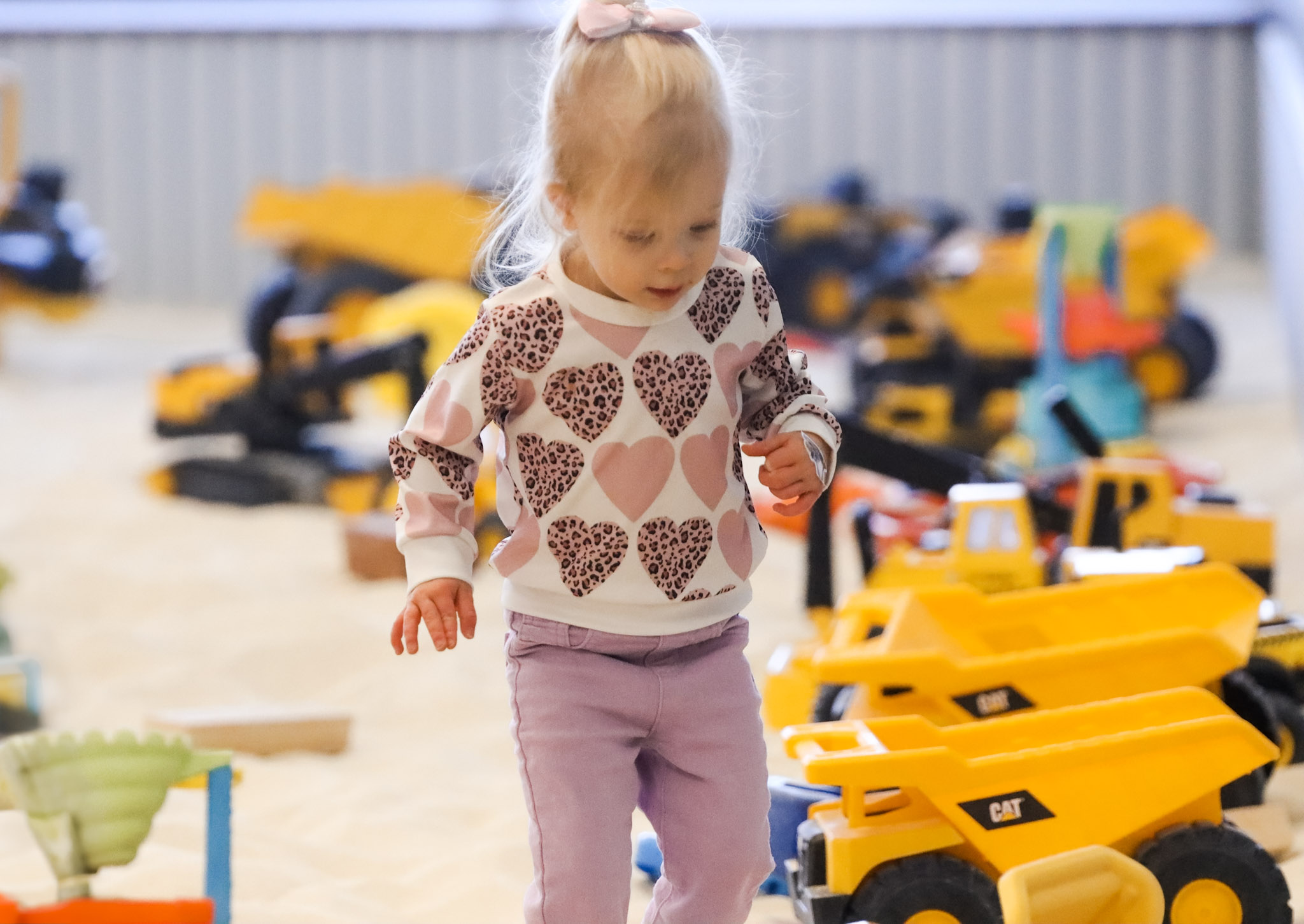 Young child driving toy construction trucks through clean indoor sand at The Sand Place in Aurora