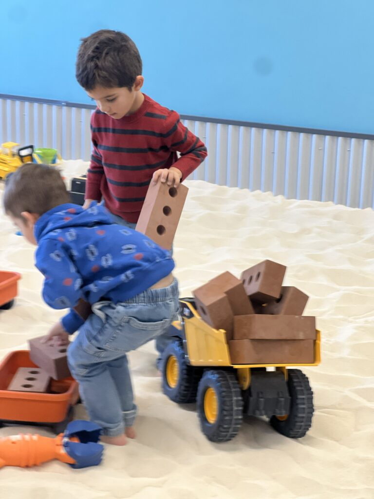 Two boys collaboratively playing with trucks in a clean, silica-free indoor sandbox at The Sand Place.
