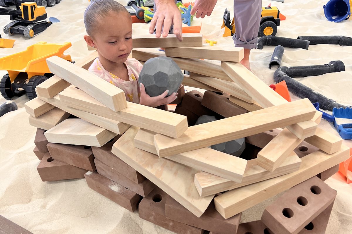 A young child building a fort out of wooden blocks and bricks in the sandbox at The Sand Place