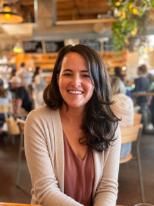 Taryn Watson of The Burrow Parenting, smiling at a cafe table in a cream cardigan